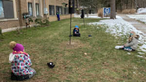 students with masks sit on the ground watching feeders nearby